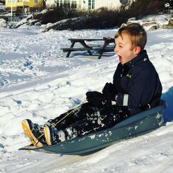 Cute boy with mouth open sitting on sled during winter