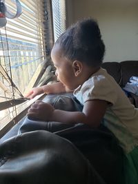 Side view of baby girl looking through window on sofa at home