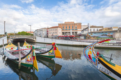 Boats moored on river by buildings in city against sky