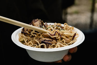 Cropped image of woman hand holding noodles in bowl