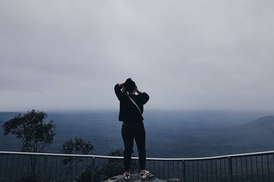 Rear view of woman photographing by railing against sky