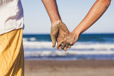 Midsection of couple holding hands on beach