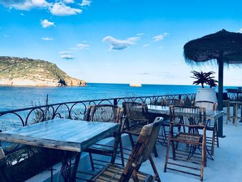 Chairs and table by swimming pool against sea against sky