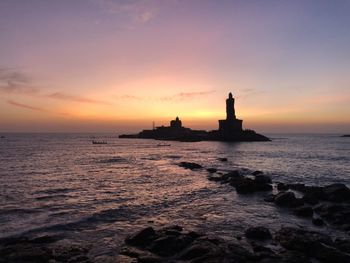 Silhouette lighthouse by sea against sky during sunset