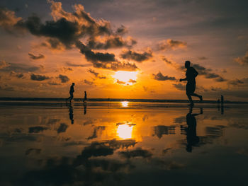 Silhouette jogging people on beach against sky during sunset