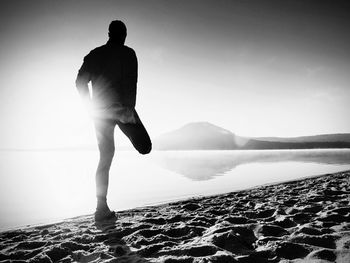 Rear view of silhouette man standing at shore against sky