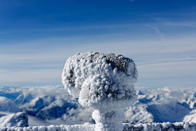 Snow covered coin-operated binoculars against sky