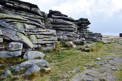 Stone wall by rocks on field against sky