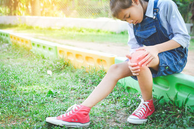 Full length of girl looking at knee while sitting on field