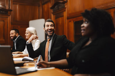 Happy businessman with mouth open sitting amidst colleagues in conference meeting at board room