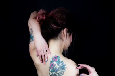 Shirtless woman with tattoo against black background