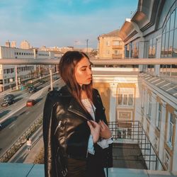 Beautiful young woman standing by railing against buildings in city