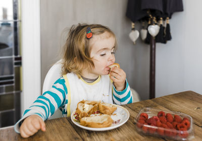 Girl eating food on table at home