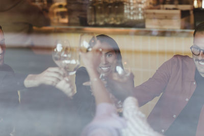 Male and female friends toasting wineglasses seen through glass of bar