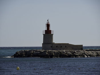 Lighthouse by sea against clear sky