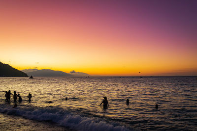 Silhouette people on beach against sky during sunset