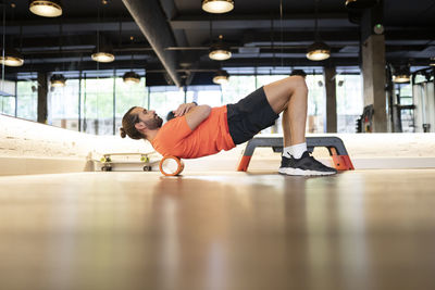 Side view of fit bearded male athlete doing back exercise on roller during fitness workout in gym