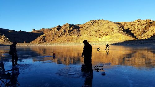 Silhouette woman standing on rock by lake against clear blue sky