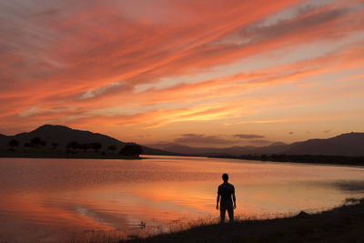 Man standing on shore against sky during sunset