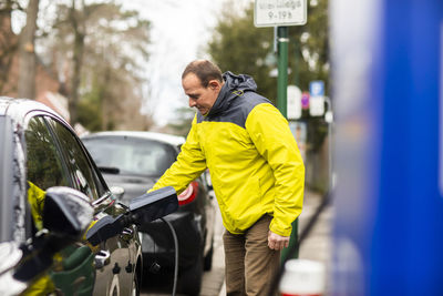 Man charging electric car with power cable at charging station