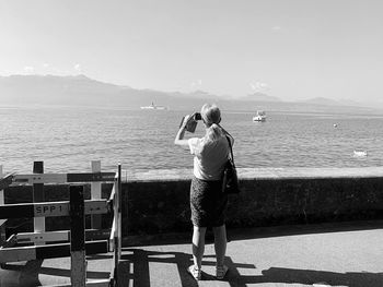 Rear view of woman standing by sea against sky