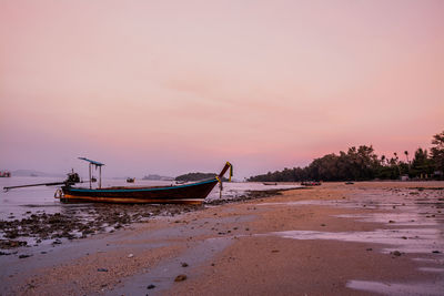 Boat moored on beach against sky during sunset