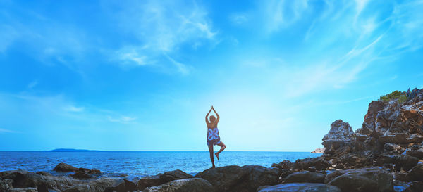 Rear view of woman standing on rock against sky