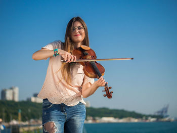 Portrait of young woman playing violin against clear blue sky