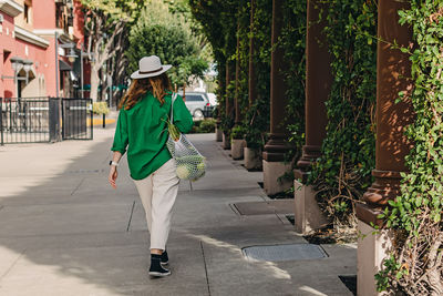 Woman in green jacket walking on the street with a bag of vegetables on her shoulder