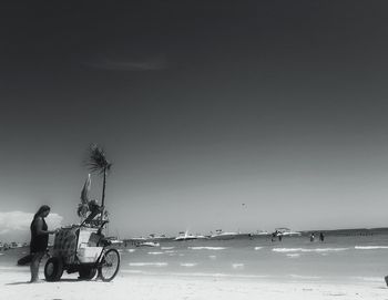 Man sitting on beach against clear sky