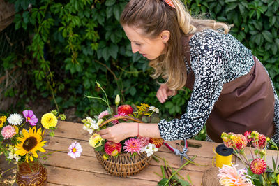 A florist girl collects a bouquet of autumn flowers in a basket on the street