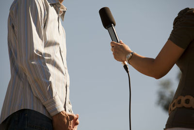 Midsection of reporter taking interview of man against clear sky