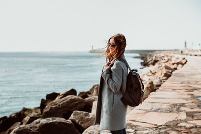 Side view of woman wearing backpack while standing on pier over sea against clear sky
