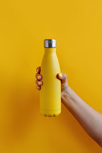 Close-up of hand holding bottle against yellow background