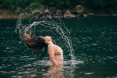 Side view of woman tossing wet hair in lake