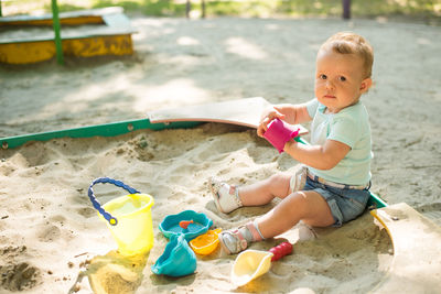 Cute boy playing with toy sitting on sand