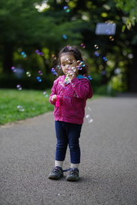 Portrait of girl blowing bubbles while standing on road