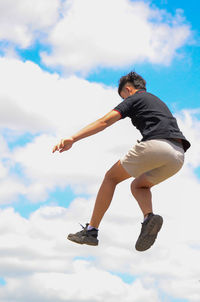 Low angle view of man jumping against sky