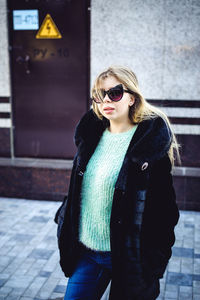 Portrait of woman wearing sunglasses standing against wall