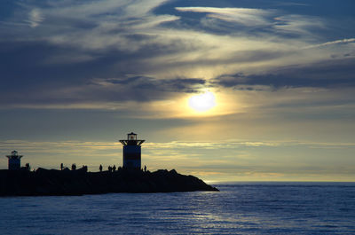 Silhouette of lighthouse by sea against sky during sunset