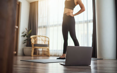 A young woman doing excercise while watching online workout tutorials on laptop at home