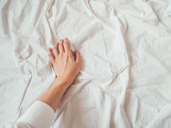 Woman's hand on background of crumpled bed sheet. creased white linen. woman touches unmade bed. 