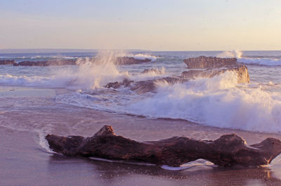 Waves splashing on rocks at shore against sky