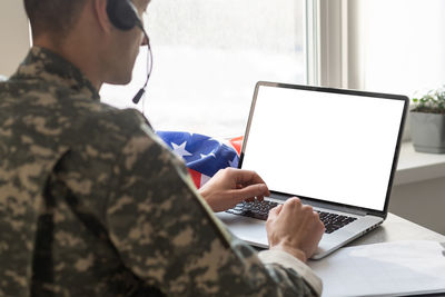 Military man gesturing in office near laptop with blank screen, usa flag.