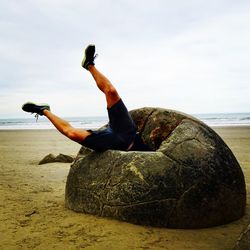 Man on rock at beach against sky