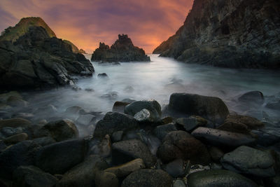 Rocks on sea shore against sky during sunset