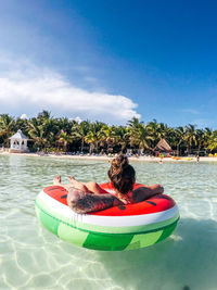 Young woman floating on inflatable ring in sea against blue sky