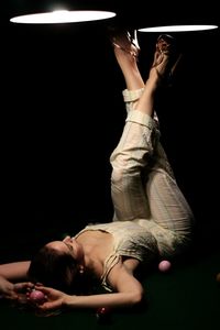 Woman with feet up lying down on pool table against black background