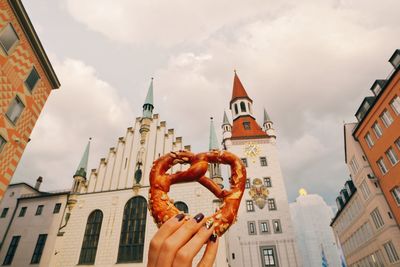 Low angle view of hand holding building against sky