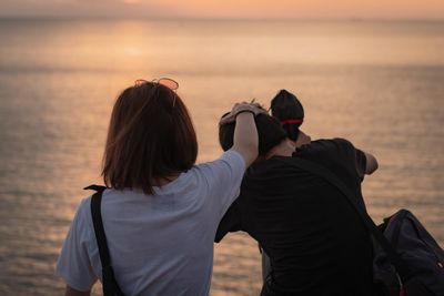 Rear view of couple sitting at beach during sunset